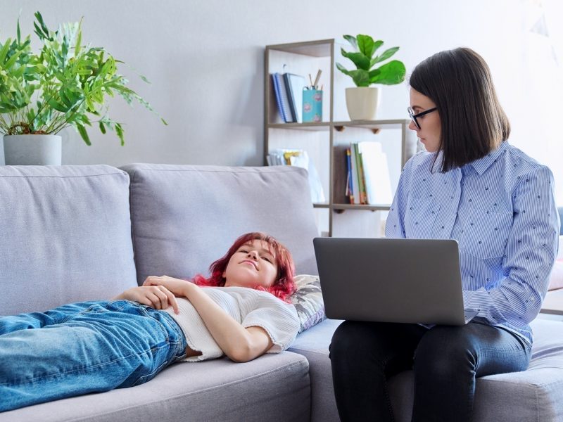 Psychologist counseling teenage female, individual therapy in doctors office. Professional behavior helping teenager, girl lying on couch. Mental health, adolescence, psychology, psychiatry concept
